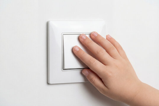 Child hand turning white light switch on white wall