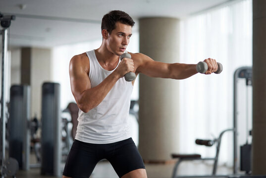 Muscular young man boxing with dumbbells in gym workout
