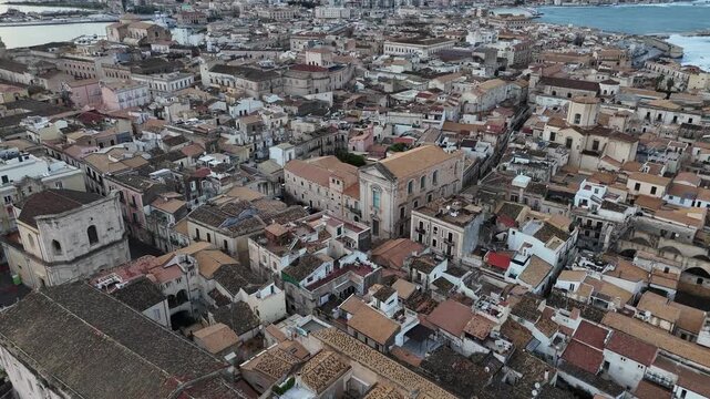Aerial drone shot over the dense rooftops of Ortigia Island in Syracuse, Sicily. High angle view of historic Mediterranean architecture, narrow streets and Italian limestone buildings