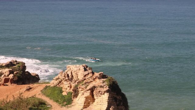 A speedboat cruising through the Mediterranean Sea near the rocky limestone cliffs of Raouche in Beirut. Scenic coastal action showing the turquoise waters of the Lebanese seaside