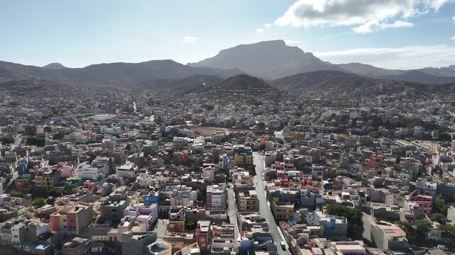 High angle aerial drone shot of Mindelo city in Sao Vicente, Cape Verde. Panoramic urban landscape featuring colonial architecture, local housing, and the dramatic volcanic mountains background