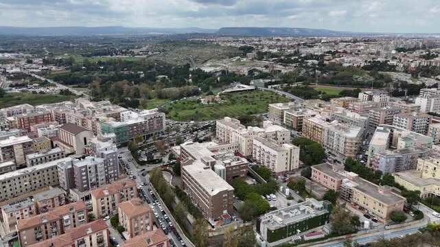 Aerial drone shot of the Santuario della Madonna delle Lacrime in Syracuse, Sicily. High angle view of the modern brutalist basilica and the surrounding urban district and green park areas