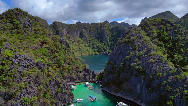 Azure waters of Barracuda Lake surrounded by lush green limestone karsts and anchored boats along the coastline. speed ramp hyper motion time lapse, Beautiful aerial view fly reverse panorama drone