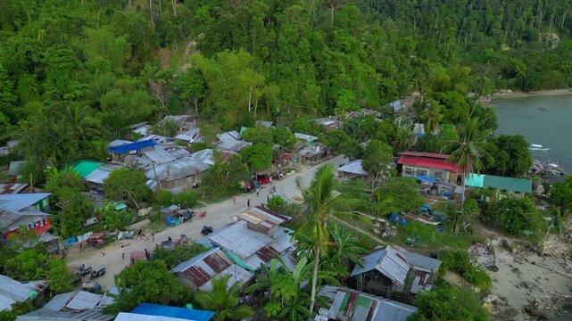 poor coastal village with children playing in the street, surrounded by simple homes and lush tropical vegetation. Smooth aerial view fly reverse panorama drone