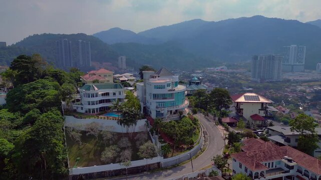 Residential properties and houses built on a tropical hillside in Penang, Malaysia, showcasing contemporary architecture and urban development. Gorgeous aerial view fly reverse panorama drone