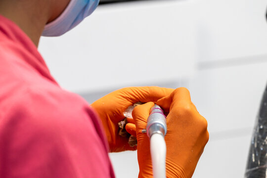 PROFESSIONAL DENTIST WEARING BRIGHT ORANGE NITRILE GLOVES, HOLDING A DENTAL AIR-WATER SPRAY TOOL