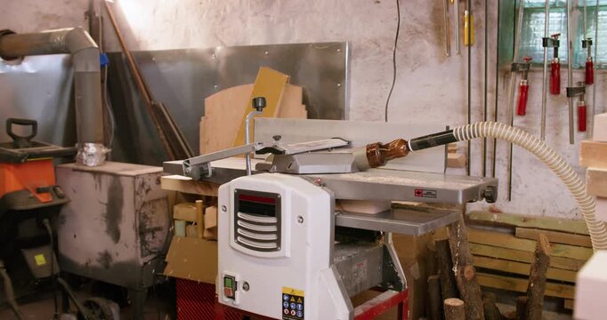 Carpentry industry. Planing wood work. Man putting piece of lumber in automatic thickness planer machine to reduce size of long block.