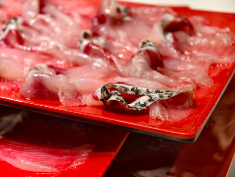 Close-up thinly sliced raw northern snakehead fish fillets on red plates