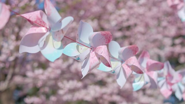 Pastel paper pinwheels hanging against a blurry background of blooming flowers