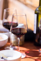 Fototapeta premium Two glasses of red wine and a bottle on a wooden table in bright sunlight
