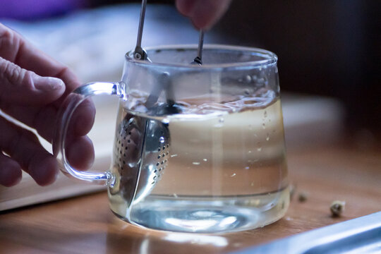 Steeping herbal tea in a glass mug with a metal infuser and a hand holding the handle