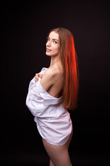 A young woman poses in a white off-the-shoulder shirt on a black background. The soft lighting highlights her relaxed and confident expression. She is wearing minimal underwear, which adds to her sens © SergeiPh