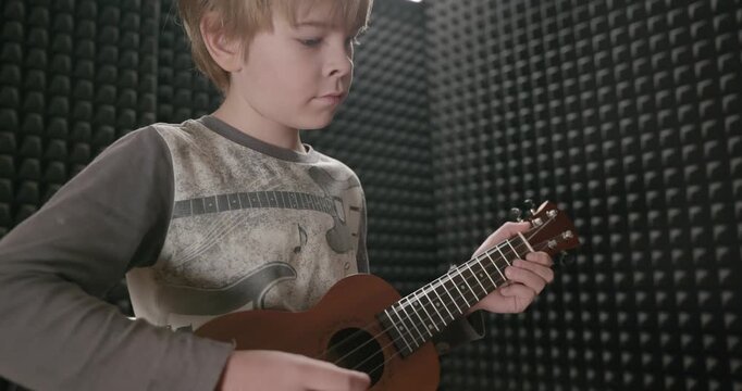 Boy Play Music on Ukulele Instrument in Home Studio. 4K 10-bit