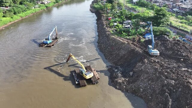 Aerial view The blue and yellow excavator is working to dig and clean the river from mud and rubbish, removing it to the edge of the river middle city 