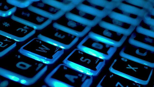 Close-up of a computer keyboard with blue backlighting in a dark environment showing buttons.