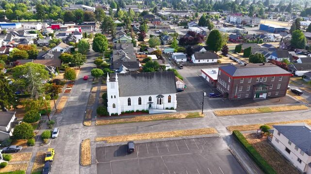 Aerial drone shot of a historic white church in Centralia, Washington, surrounded by residential houses with a scenic city view under a sunny summer sky.