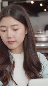 Vertical Screen : Young Asian freelance women working on laptop at coffee shop. Asian happy girl barista waiter wear gray apon serve hot cup of coffee to female customer who business work in cafe.