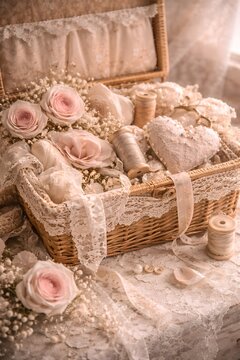 Geflochtener Korb mit Spitzenstoffen, Garnrollen, Rosen und nostalgischen N&auml;hdetails.