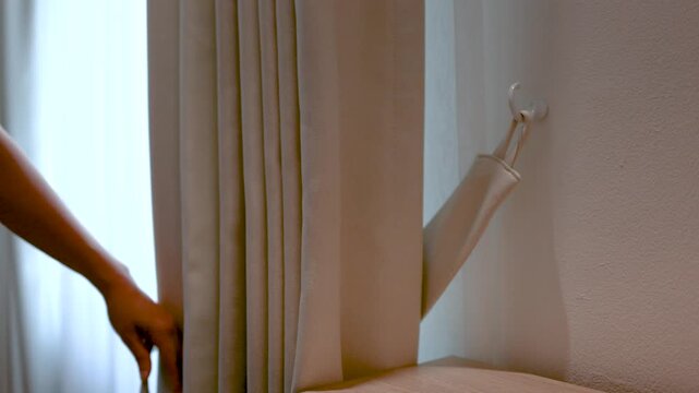 Woman Untying Curtain Tieback and Closing Drapes in Home Interior
