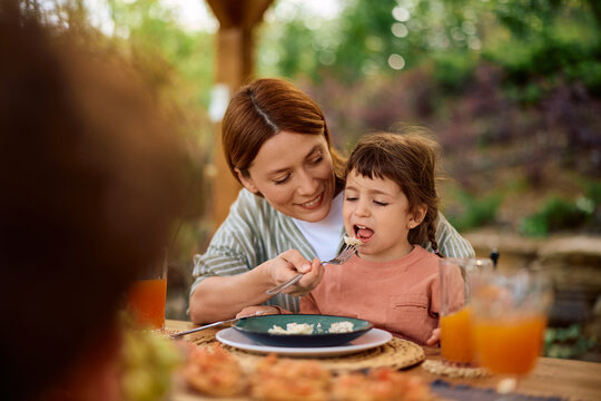 Happy mother feeding her daughter during family lunch on terrace.