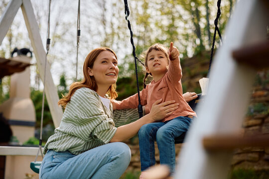 Happy mother and daughter swinging in backyard.