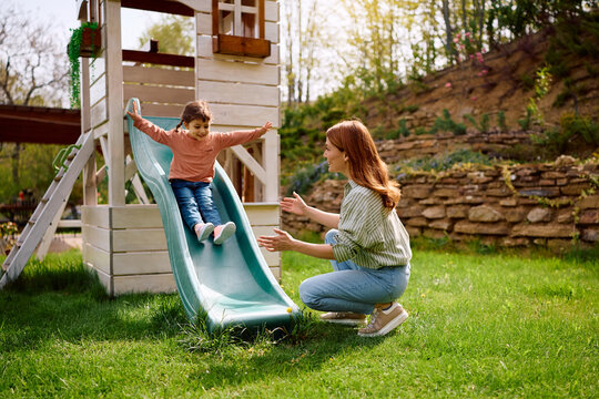 Happy mother and daughter having fun on playground slide at park.