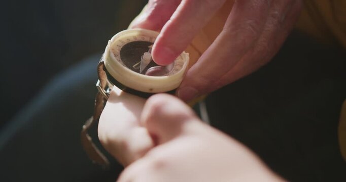 Close up view of adult hands adjusting vintage wrist compass on child arm, showing navigation teaching moment with focus on guidance, learning, and outdoor exploration