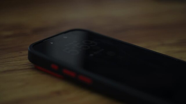 Smartphone alarm clock showing 6:00 on screen. Early morning wake up concept with mobile phone in dark room