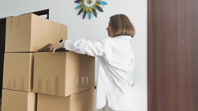 Longterm storage and organizing boxes feature woman sealing cardboard containers in apartment. Bright space contains stacked supplies for future relocation. Longterm storage helps organizing boxes.