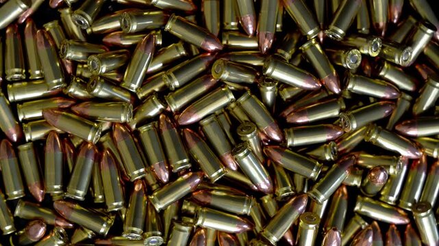Pile of 9mm bullets rotating in circular formation. Close up top down view of ammunition cartridges spinning with metallic shine