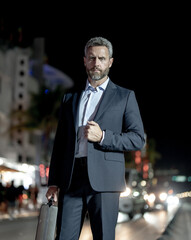 Businessman with briefcase walking at night city. Rich man in suit in city. Businessman near luxury...