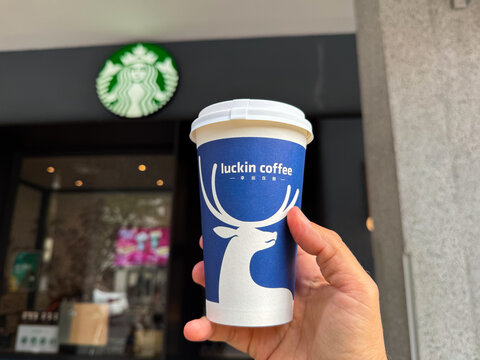 Shanghai, China - November 24, 2025: Luckin Coffee Cup Held in Front of Starbucks Logo