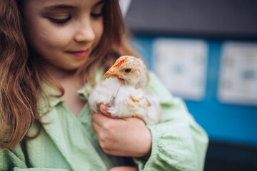 Child gently holding baby chicken, playing in garden during spring. © Halfpoint