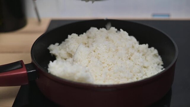 Rice is poured into a frying pan where it will be cooked. The process shows how to prepare rice quickly and easily in a home kitchen setting