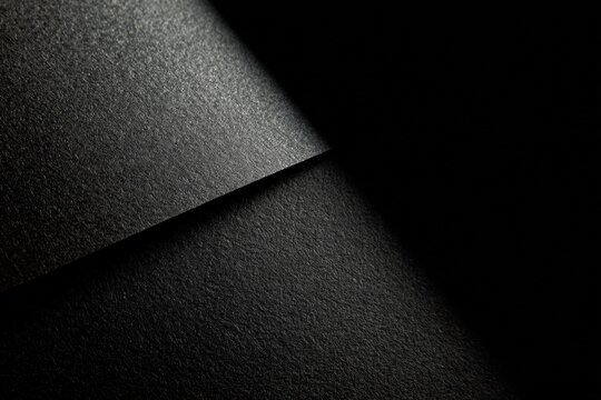 Abstract image showcasing textured surfaces in varying shades of black, with light creating contrasting shadows.