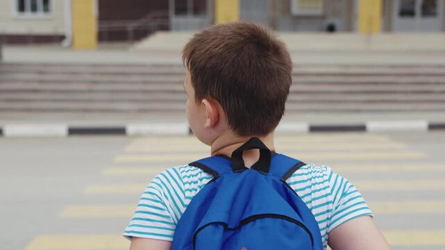 Schoolboy pauses at zebra crossing watching passing car closely, Young student at intersection waits for vehicles to clear, Child checking traffic before crossing street near school gate, Kid with