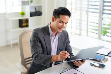 Fototapeta premium Confident young businessman auditing revenue report and planning budget while working at desk in office.
