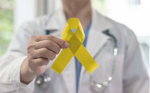Yellow awareness ribbon for Sarcoma Bone cancer, Adenosarcoma, Bladder cancer, Liver disease, Spina Bifida Awareness Month and suicide prevention in doctor's hand