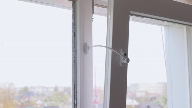 Static tripod shot of a white plastic window opened with a child safety cable lock