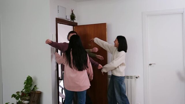 Joyful young friends warmly welcoming and embracing each other at the front door of a home