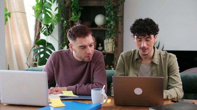 Two young male partners working and studying together on their laptops in a cozy home office