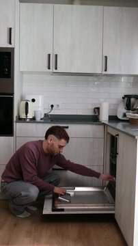 Domestic chore concept showing a man taking out clean dishes from a modern dishwasher at home