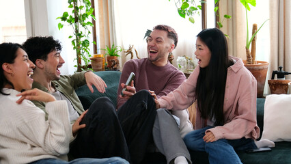 Obraz premium Group of happy young friends enjoying shared content on a mobile phone on a couch at home