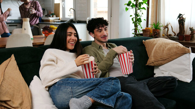 Couple relaxing on sofa, watching film and eating popcorn, sharing a happy moment
