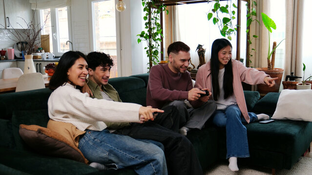 Happy young adults playing video games together on a couch at home