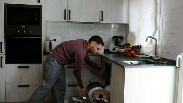 Man performing daily house chores by loading a dishwasher in a contemporary kitchen