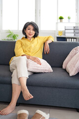 Obraz premium Positive mature woman with smile sitting on cozy couch, happy middle aged female looking at camera enjoying leisure time, relaxing on sofa alone.