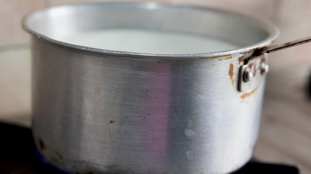 Aluminum pot with milk heating on a stove in an Indian kitchen. Daily cooking routine, simple household scene, rural lifestyle, poverty, slum village poor india concept.  