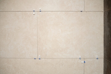 Fototapeta premium Large beige porcelain wall tiles recently installed with spacers and leveling clips, showing modern construction process and precise interior wall cladding.