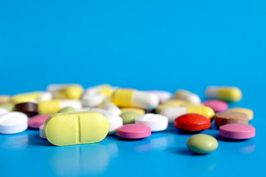 There are many multi-colored medicine tablets on a blue background.